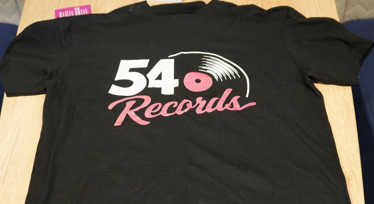 A 54 Record branded black T shirt laid out on a desk