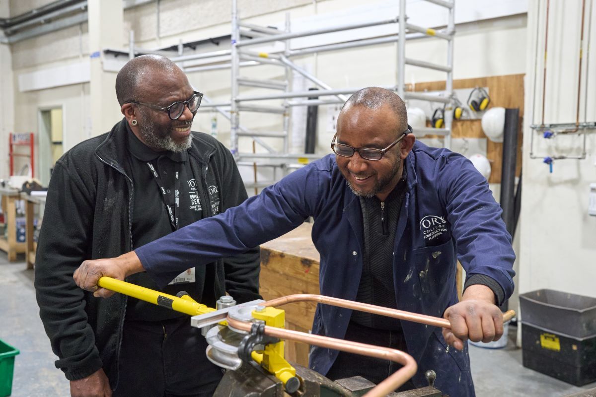 A Plumbing student bends a metal pipe while a tutor looks on Courses for Adults