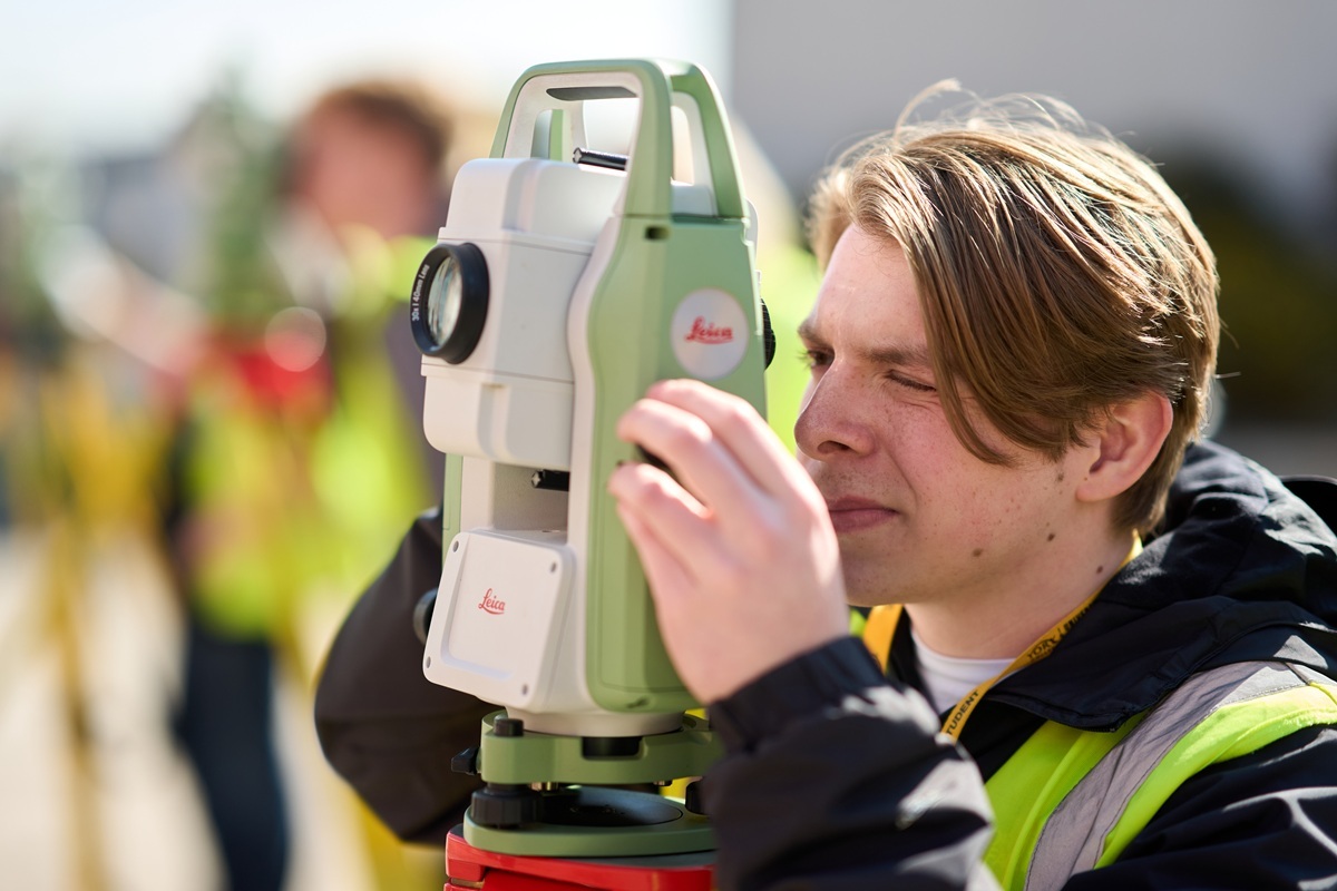 A construction student is using surveying equipment