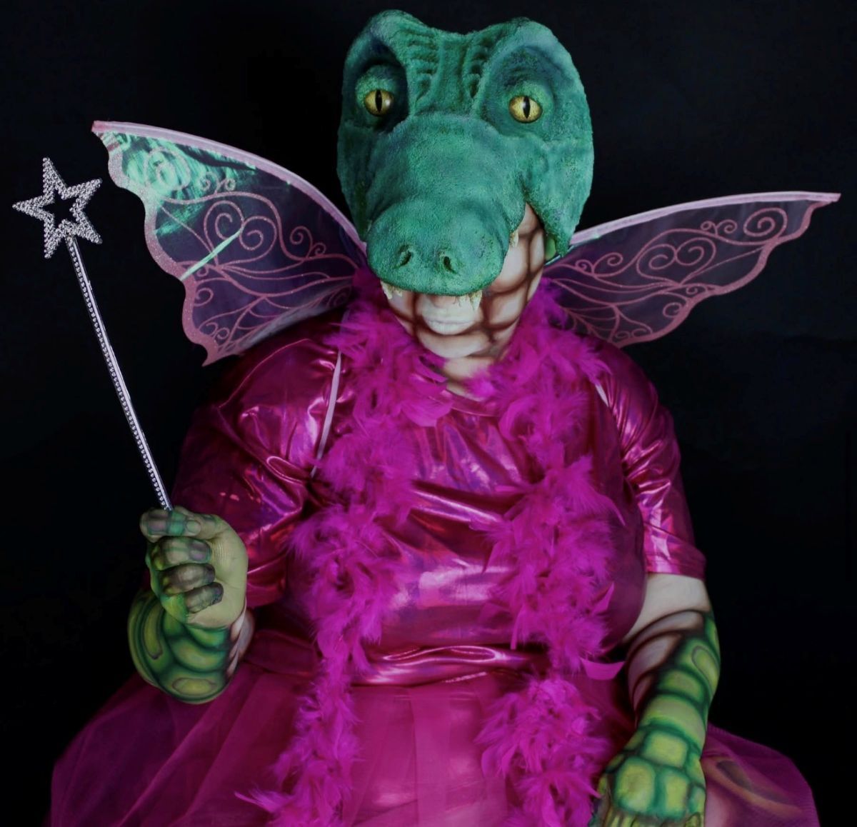 A crocodile dressed in a pink fairy godmother dress with a wand and wings on its back