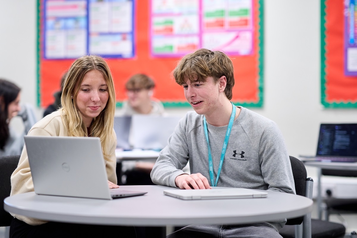 A female and male student both smiling looking at the screen on a laptop