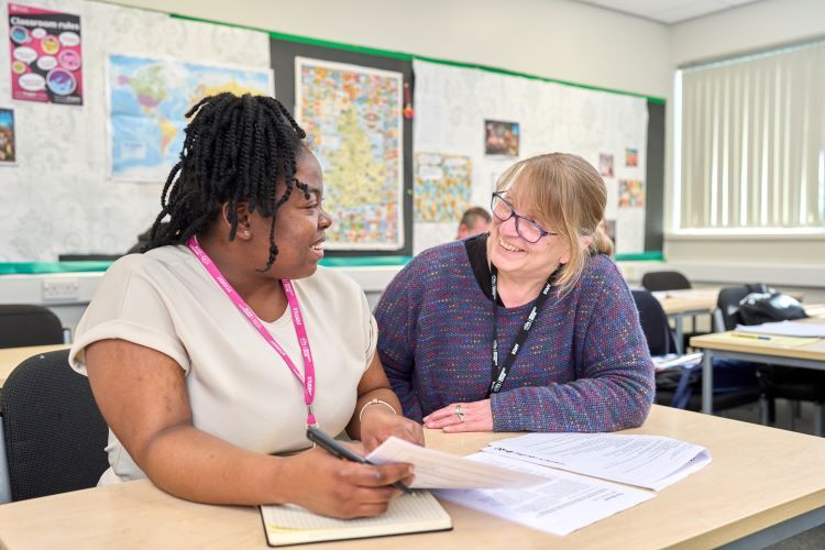 A student and a tutor smile at eachother as they discuss the work