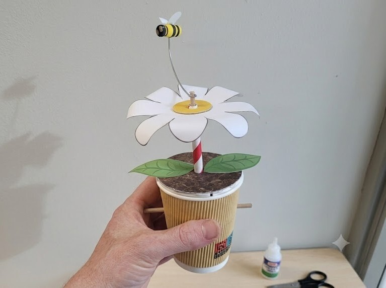 A student holds up a plan pot automata with a flower in it