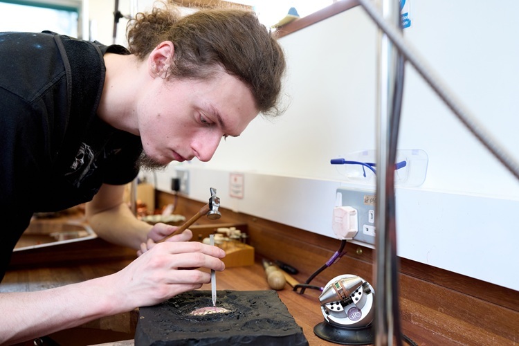 A student uses a small chisel or saw on some metal Jewellery