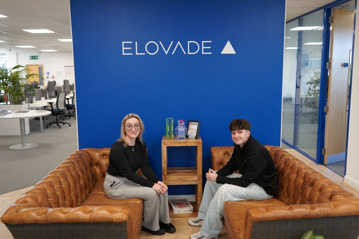 Amy Abba and Josh Jenkins sit on opposing leather sofas in front of Elovade branding in their Thirsk office