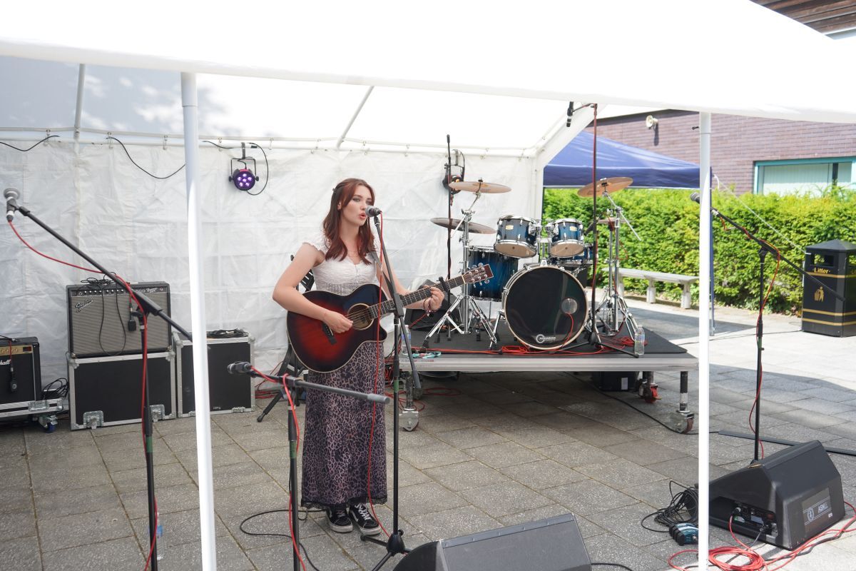 Daisy Summers singing and playing guitair under a marquee at York Colleges Welcome Fest Celebration