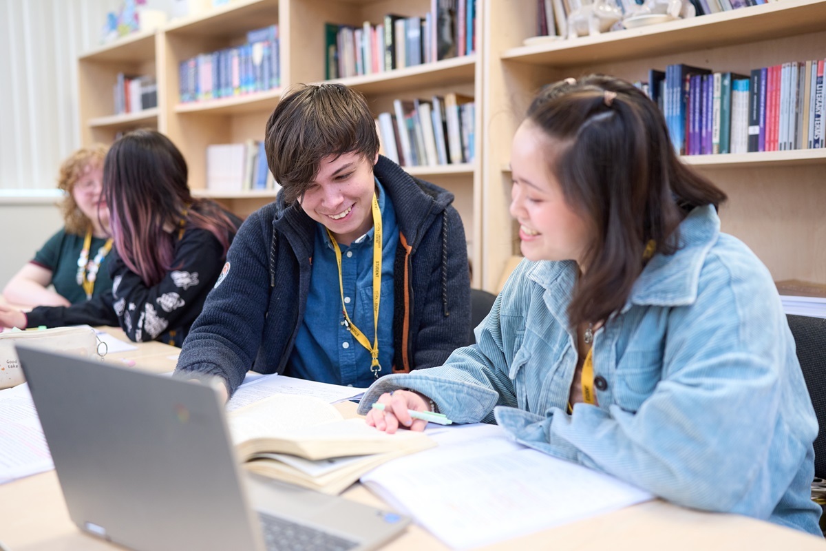 English Literature students seated together looking at a book and discussing the content