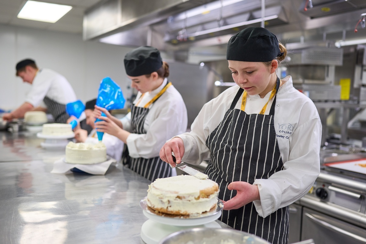 Four student chefs are working in a row in the training kitchen icing cakes
