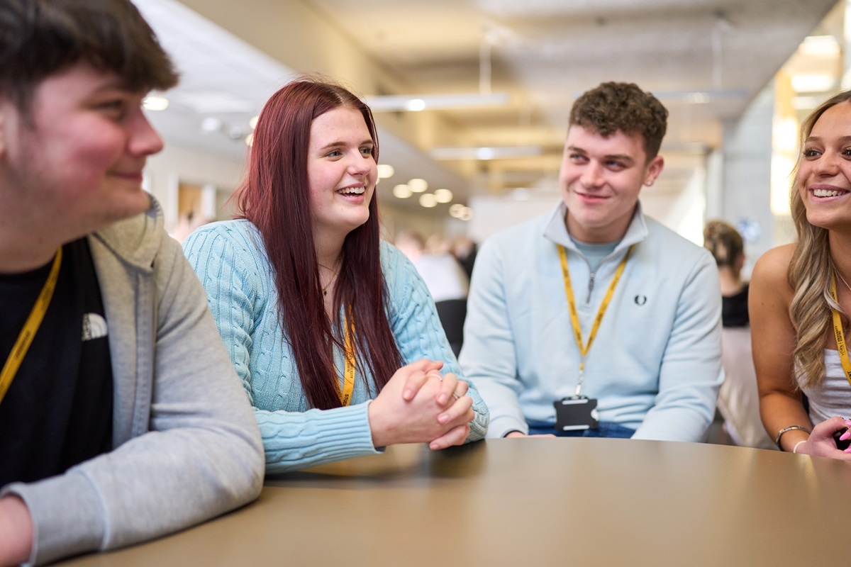 Four students talking and laughing around a table in the learning centre
