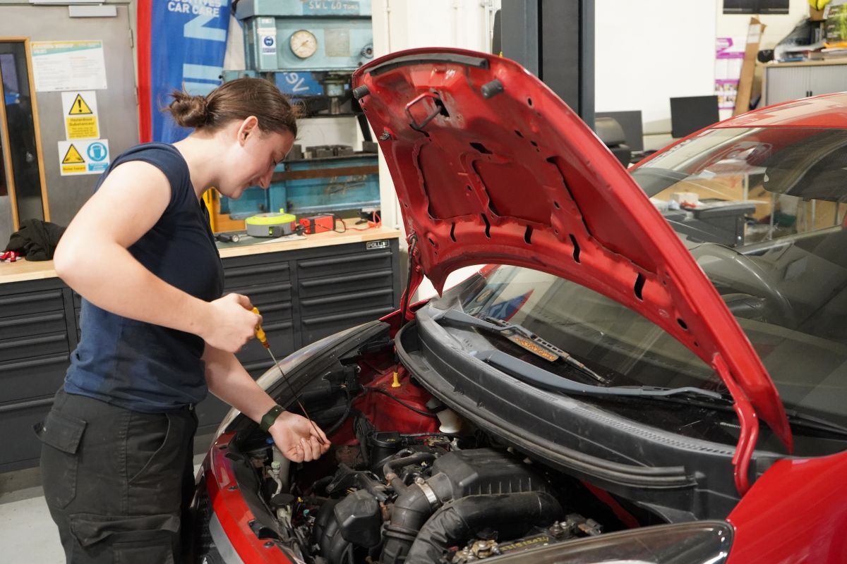 Georgina Richardson checks the engine oil under the bonnet of a red car in the York College Motor Vehicle workshop