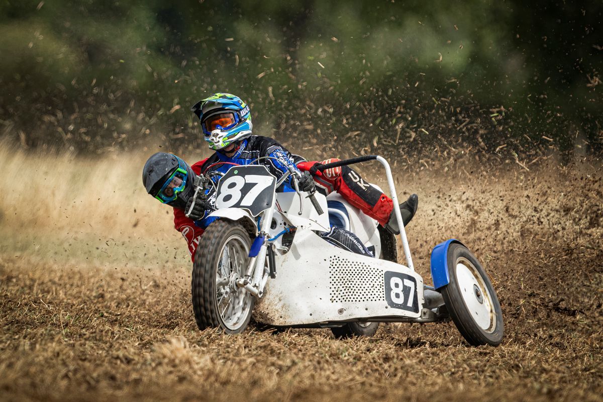 Georgina Richardson hanging off the back of a sidecar as the driver goes a round a courner with mud and grass flying up
