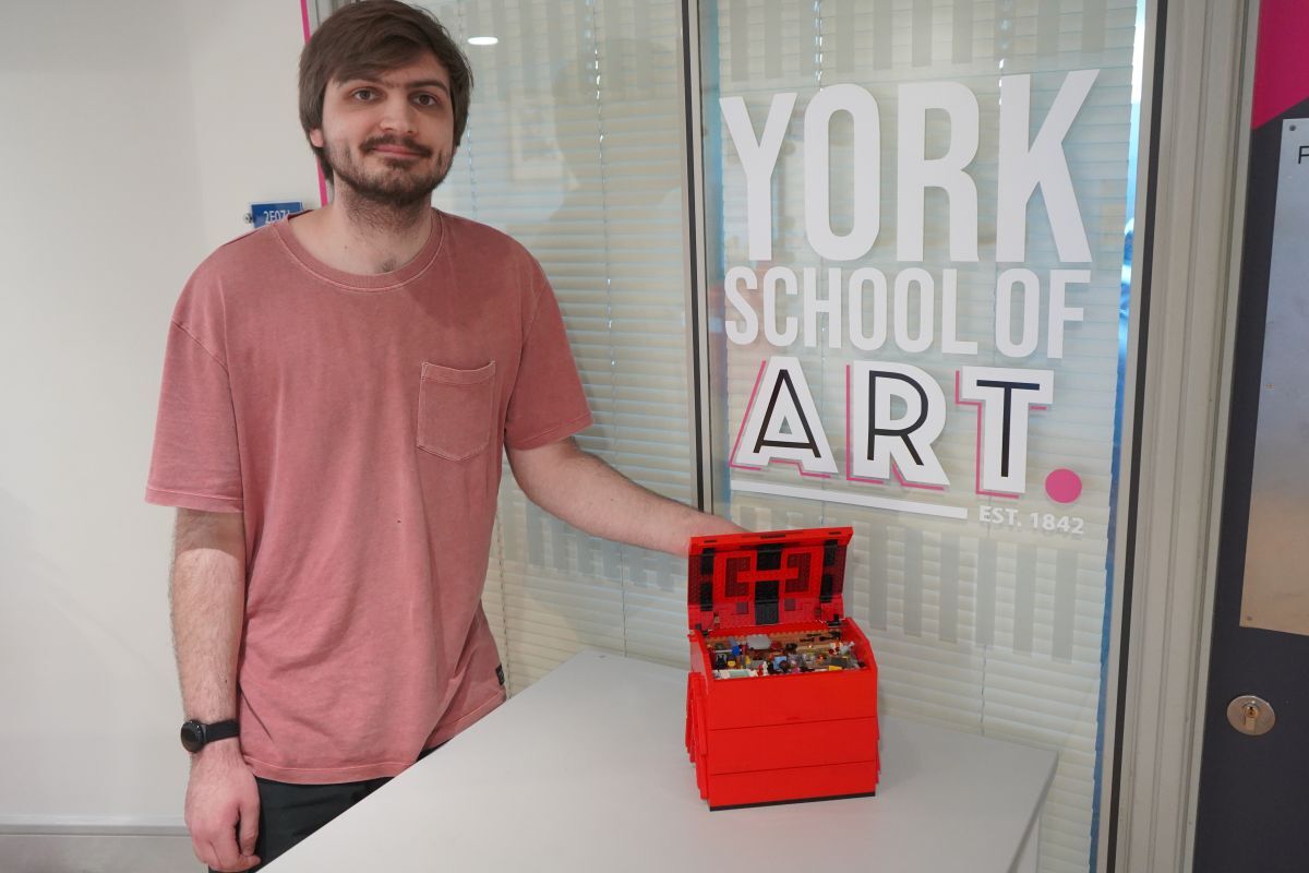 Joe Bailey poses with his Workshop in a Toolbox Lego set in front of York School of Art branding
