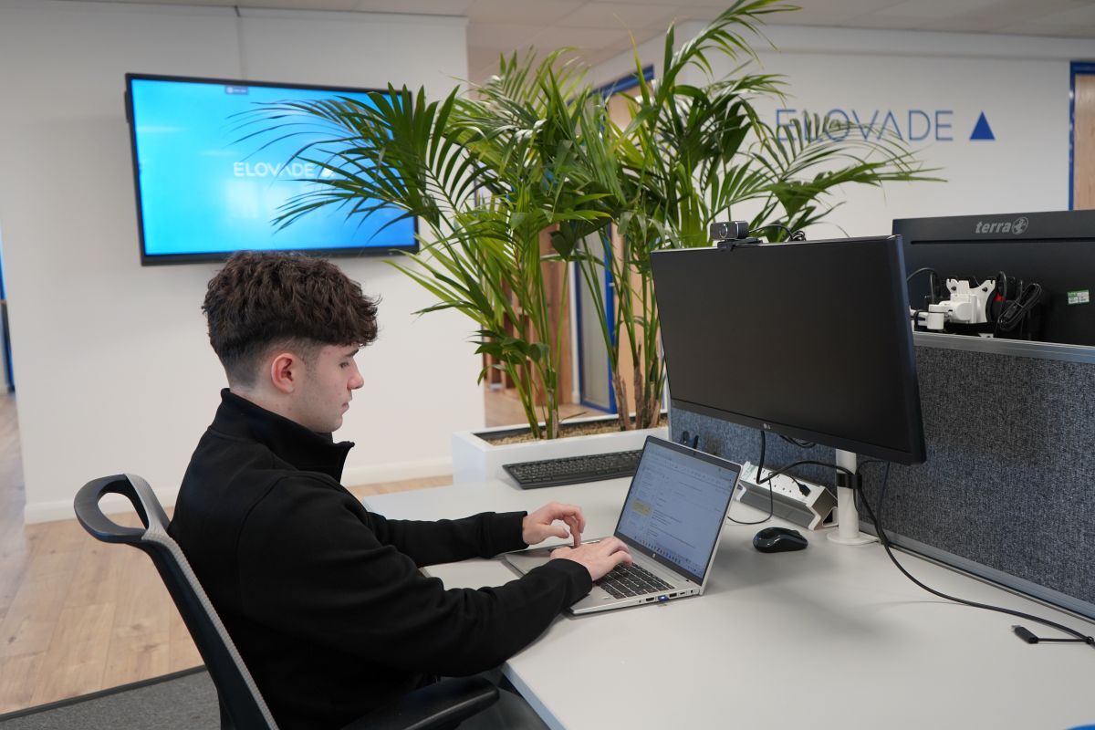 Josh Jenkins works at his desk with Elovade branding on the wall and a TV screen in the background