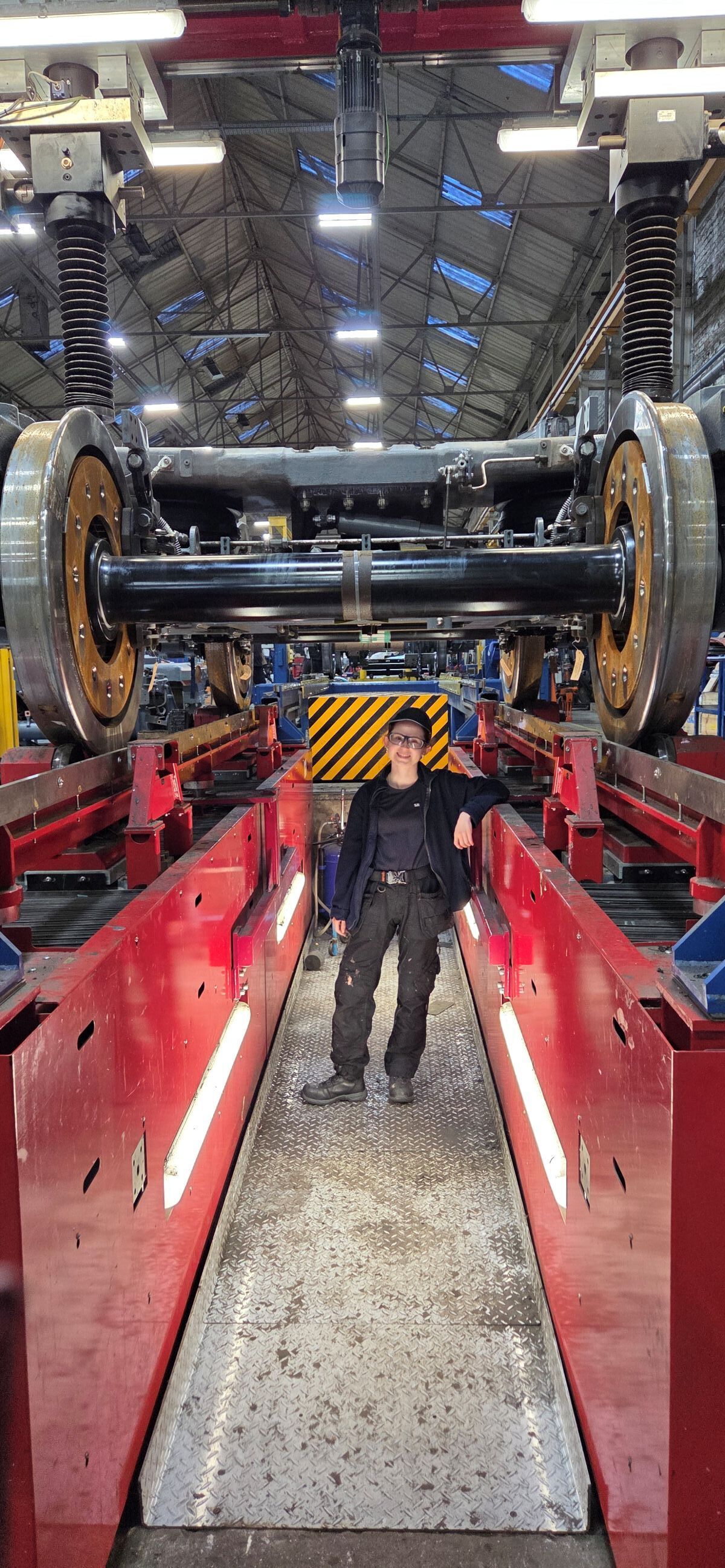 Robyn Bradley in a pit working underneath a suspended pair of large train wheels