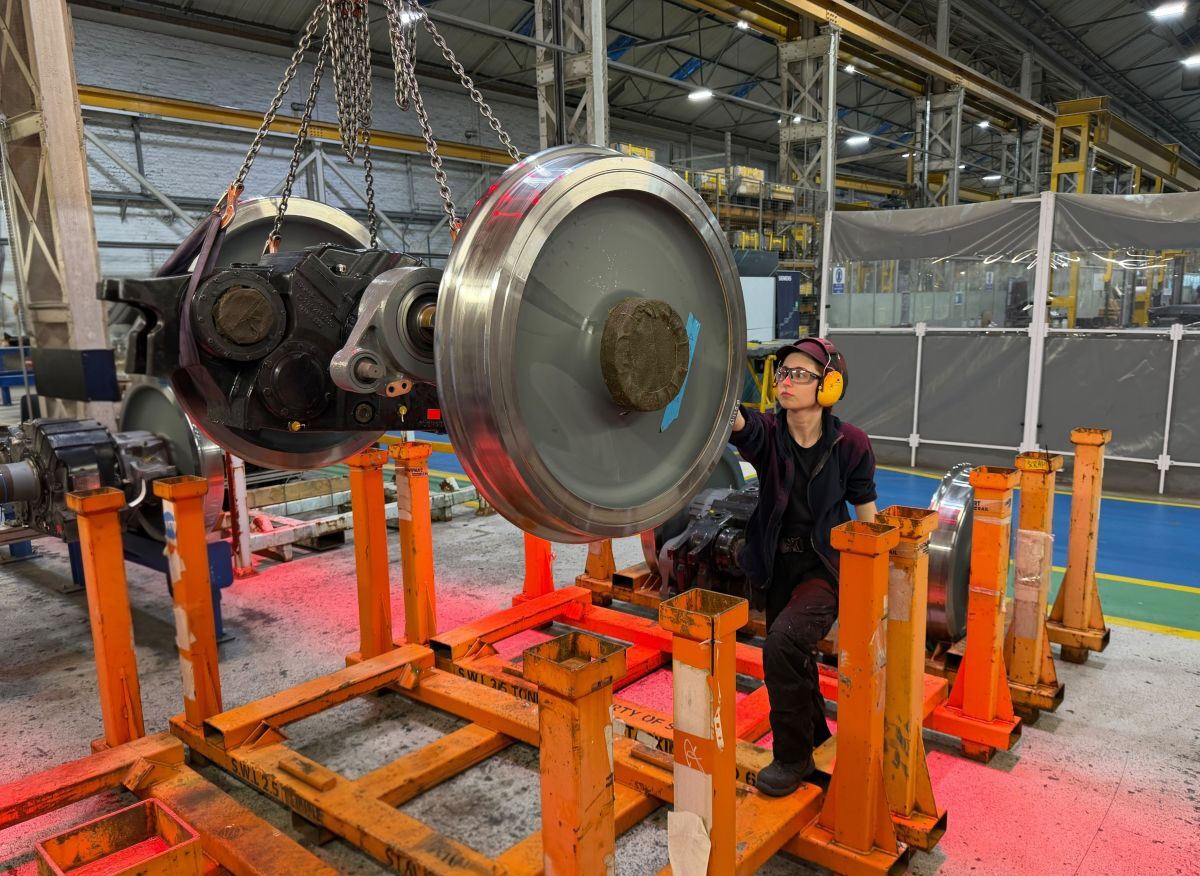 Robyn Bradley works on a big pair of train wheels while wearing overalls and ear protectors