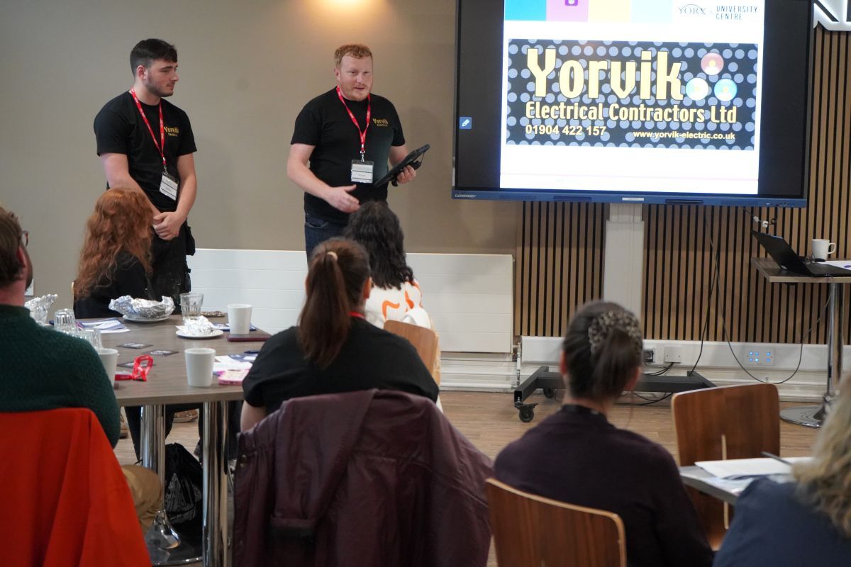 Ryan Watson of Yorvik Electrical addresses and audience in The Cookery with Case Gilmore stood next to him and both next to a big screen with the company logo on it