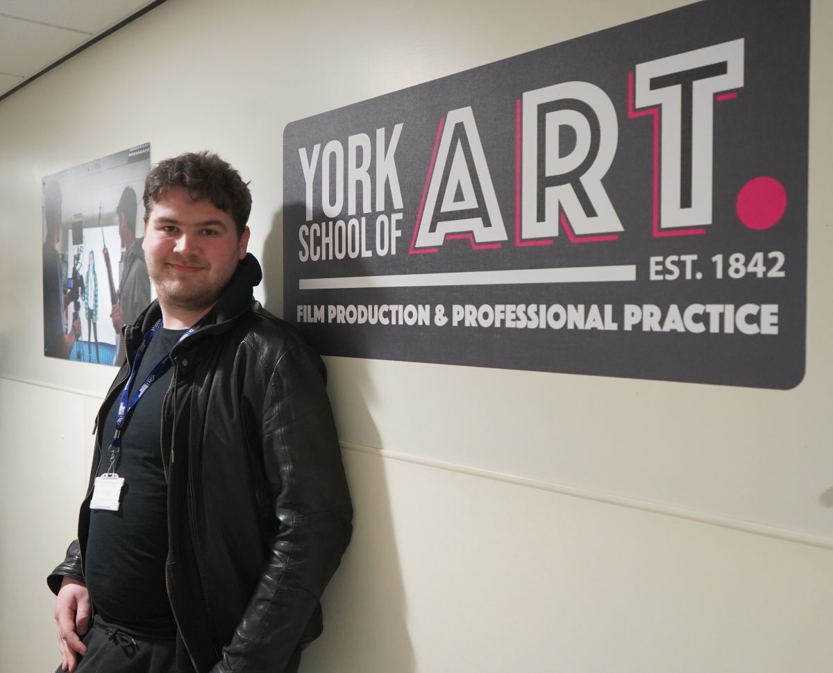 Sam Matten poses in front of York School of Art branding