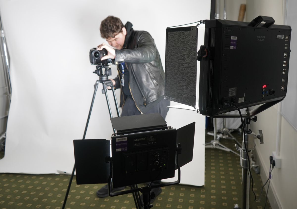 Sam Matten sets up a camera on a tripod in front of a white screen with two sets of lighting equipment