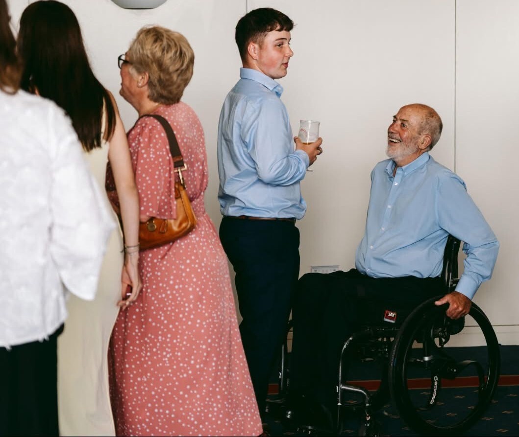 Sam Welch holds a drink while talking to his granddad in a wheelchair in the reception area at the REACH Awards