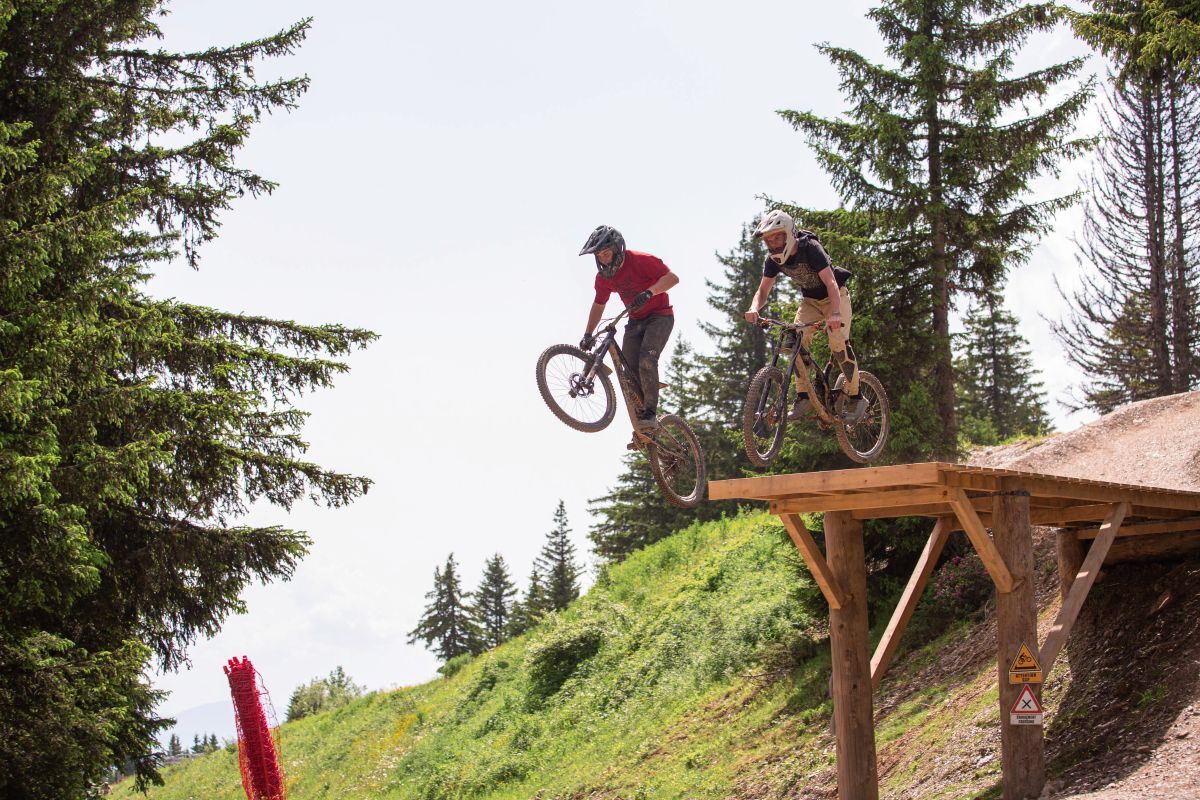Sam Welch just leaving wooden podium on his bike with front wheel up in Morzine with trees in background