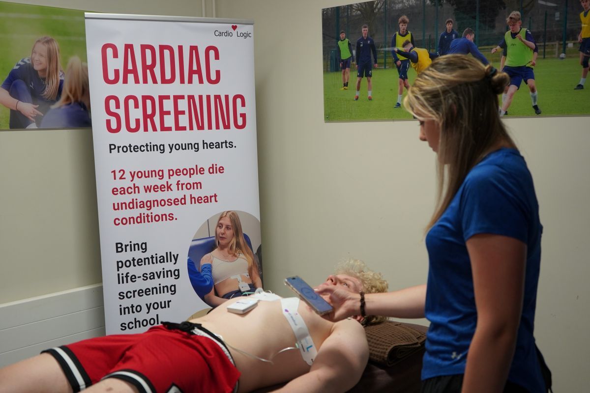 Sports tutor Emma Palmer looks at readings on her mobile phone device as student lies on the patient bed with ECG electrodes attached to his chest