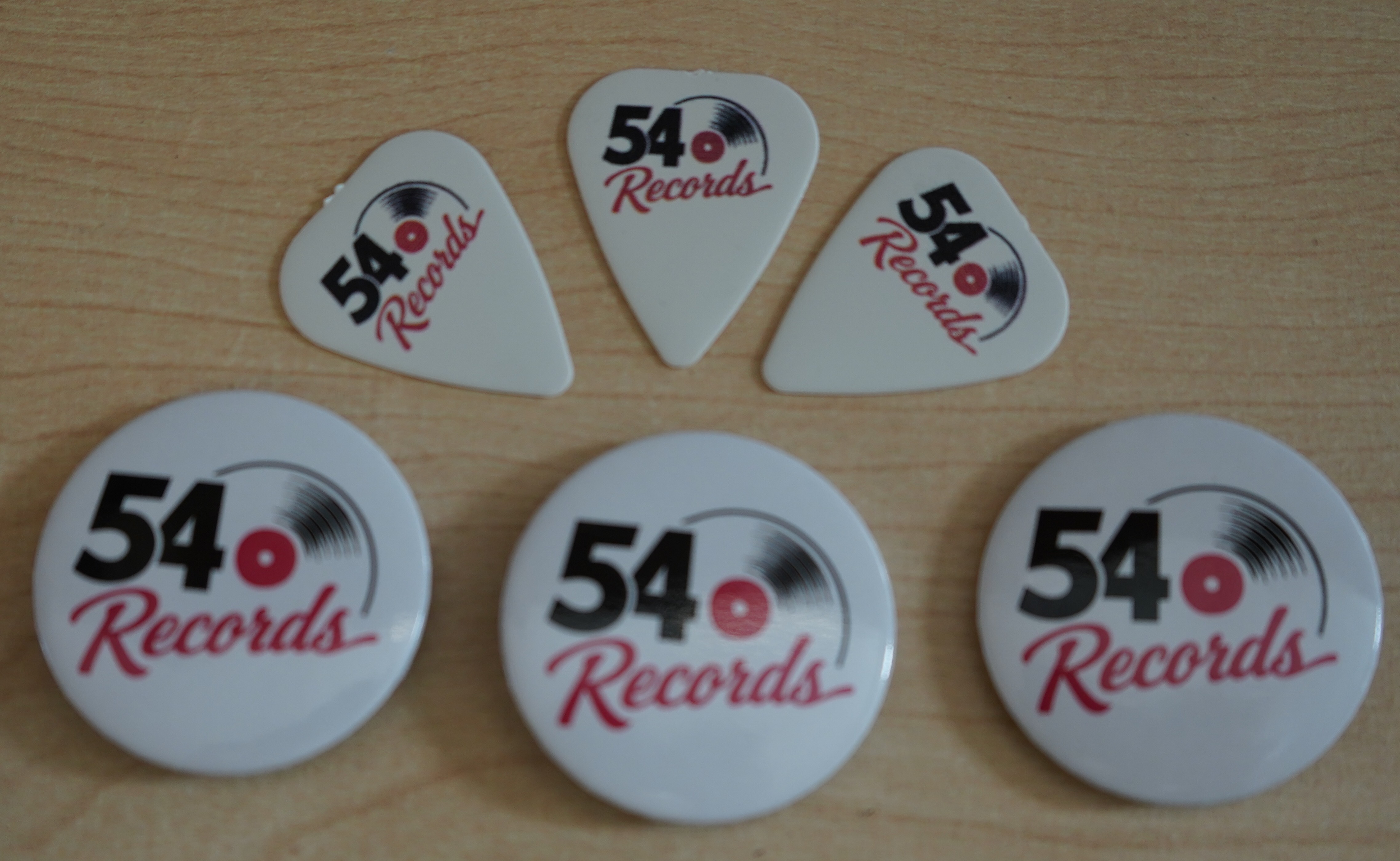 Three 54 Records branded guitair picks above three 54 Records branded badges on a desk