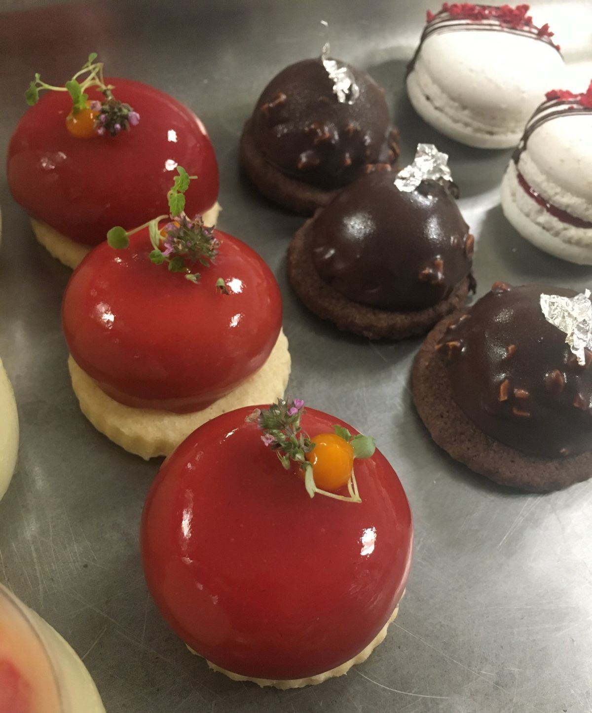 Three red glazed macarons with dark chocolate and white ones in the background
