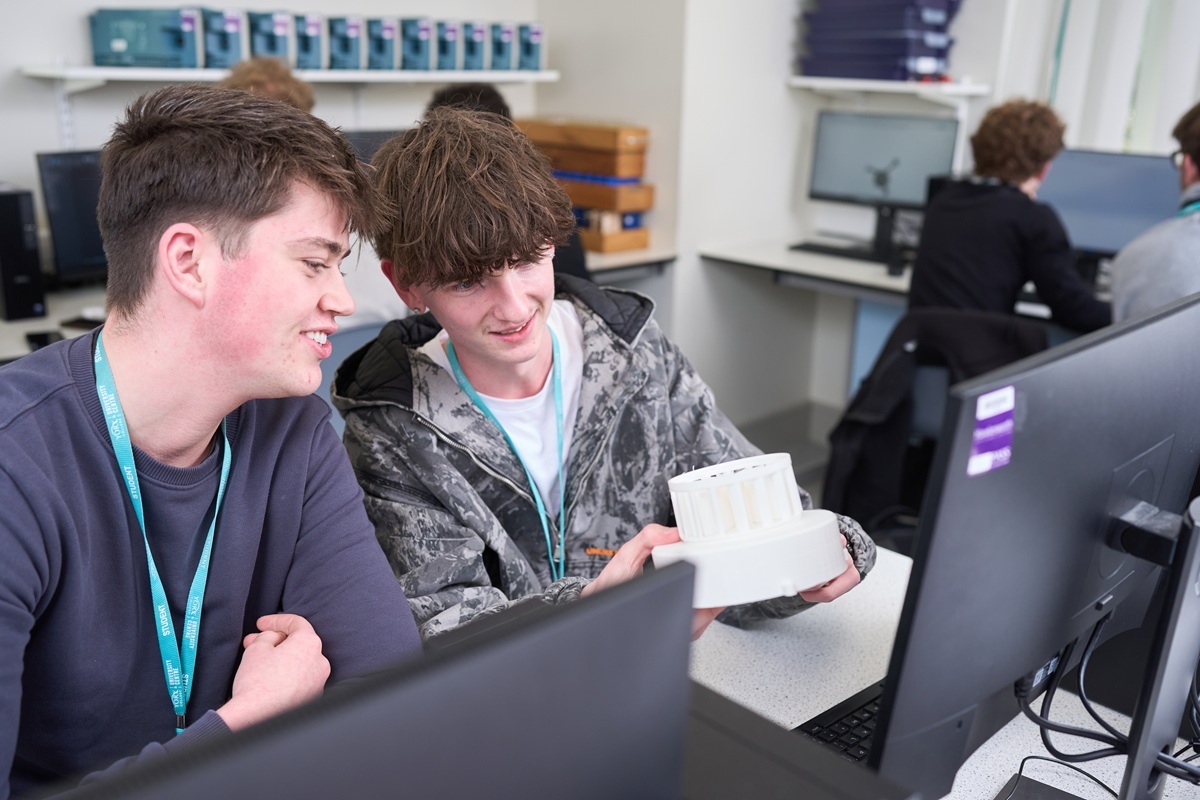 Two engineering students discuss a 3 D printed object compared to the design on the computer screen