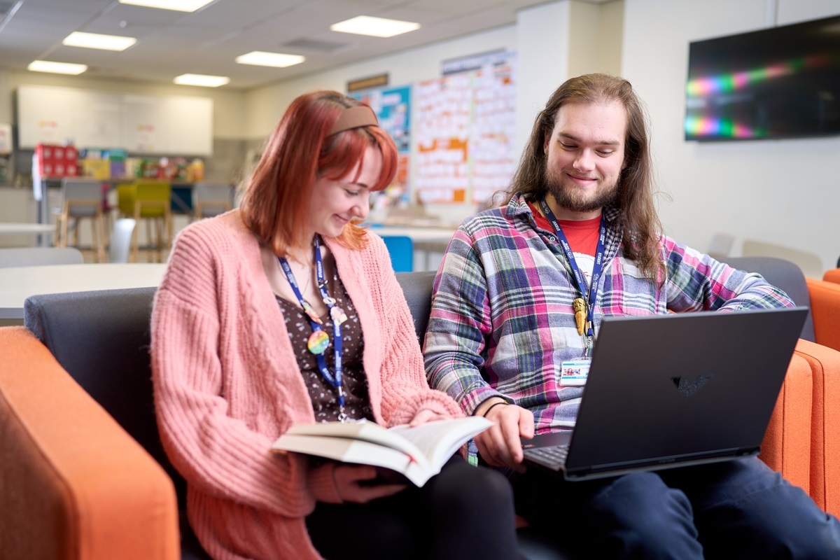 Two students chat one reads and one works on a laptop Request a prospectus