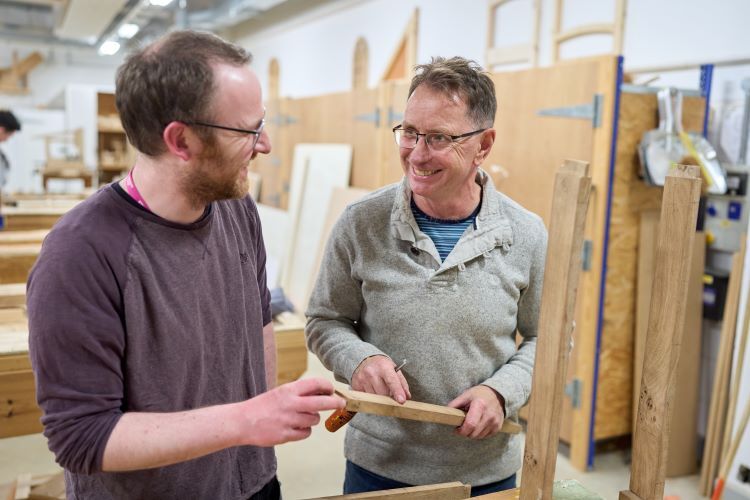 Two students mark up some wood and smile