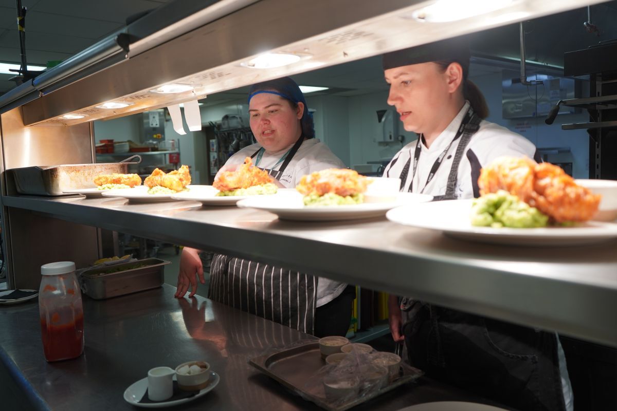 Valentina Zarins and a student look at order slips behind a hot plate with fish and chips ready to be collected and served from York Colleges The Cookery kitchen
