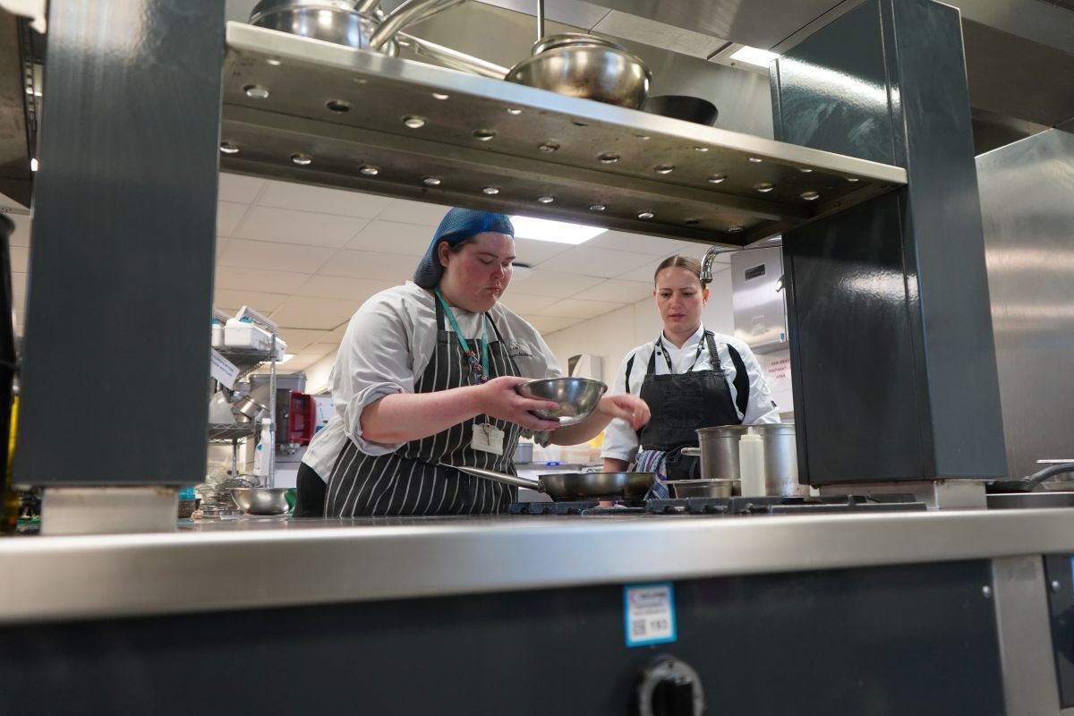 Valentina Zarins assists a female student at a hob with pans on it