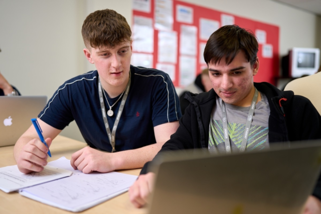 Two students looking at a laptop working in the business classroom