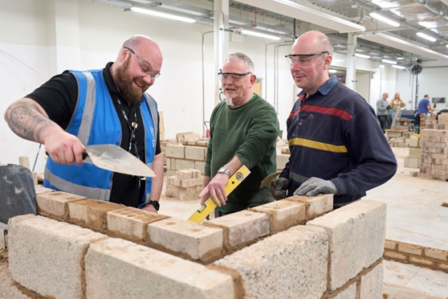 A tutor guides two students in building a wall