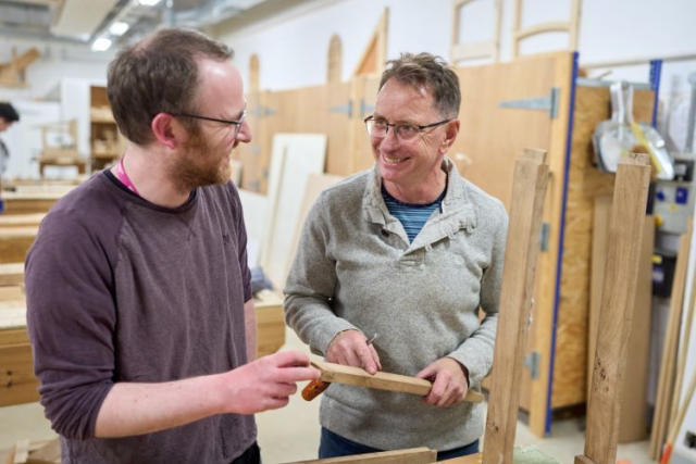 Two students mark up some wood and smile