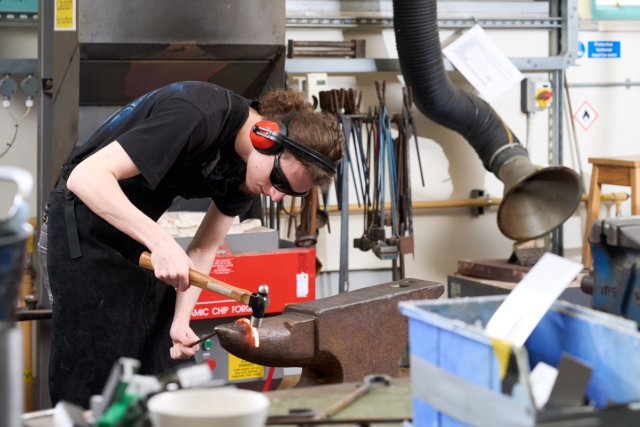 A student hammers some metal on a forge 3 D