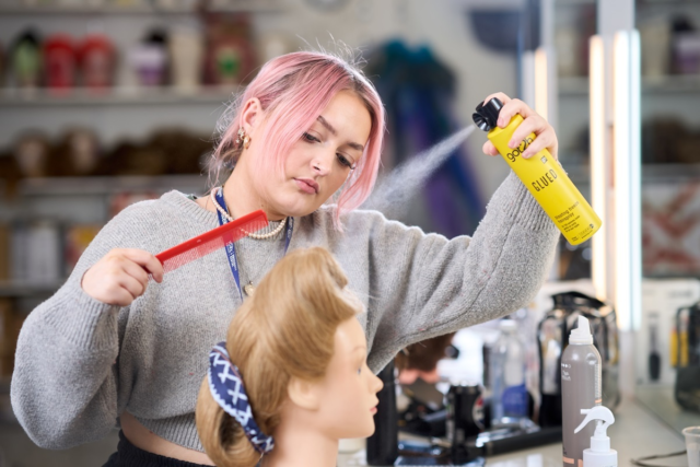 A student sprays some hairspray on a wig Media Makeup