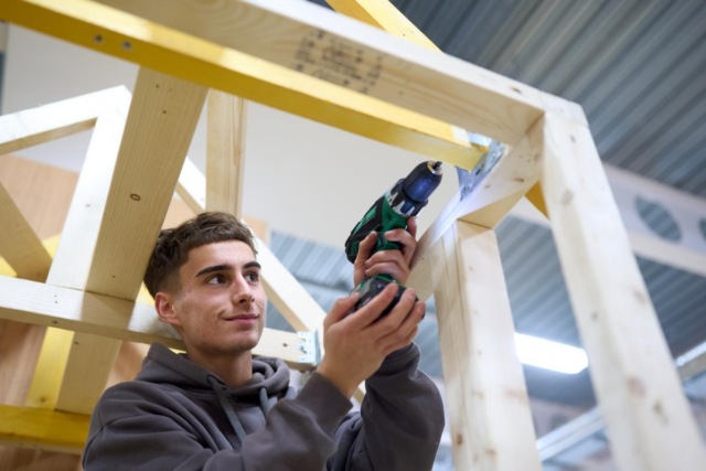 Male student drilling woodframe