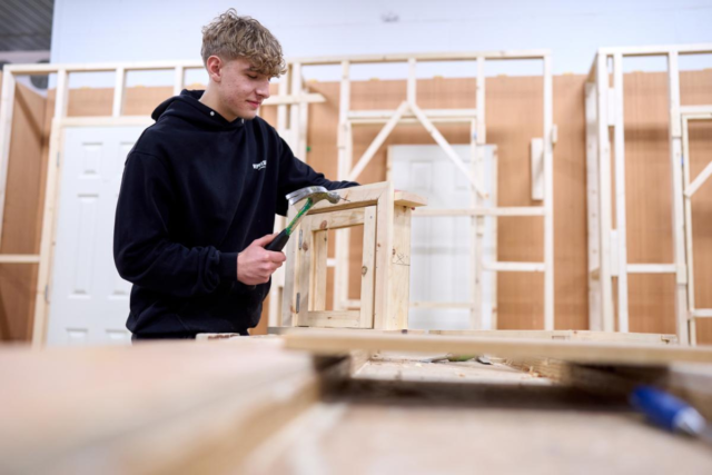 Male carpentry student hammering wooden frame