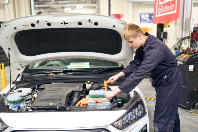 Motor Vehicle student leaning over the engine of a car making adjustments with a spanner