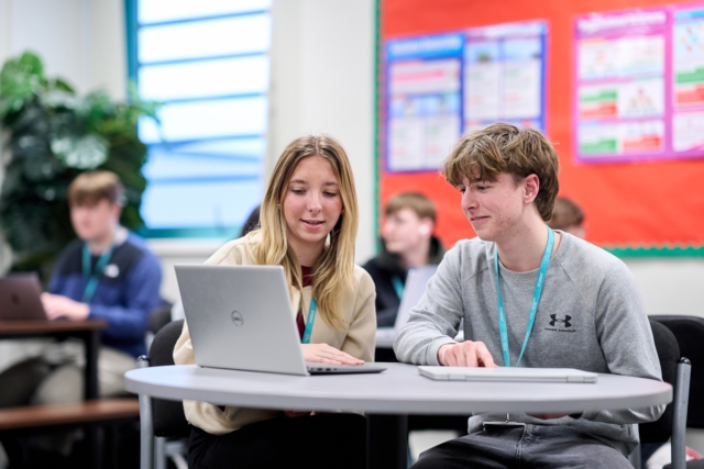 Business students sitting at a round table discussing work they see on the laptop in front of them
