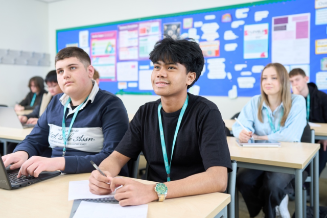Business Level 2 students sit at desks with notes and laptops looking towards the front of class