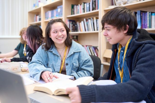 Two A Level English students sitting at a desk smiling as they discuss the book in front of them and make notes