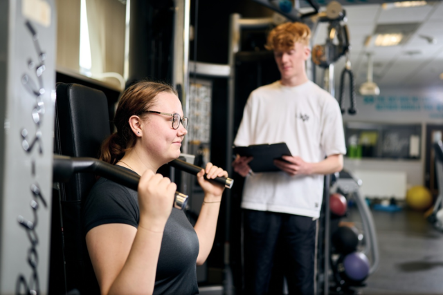 A sport student is instructing another in how to use the gym equipment in The Athletic Suite