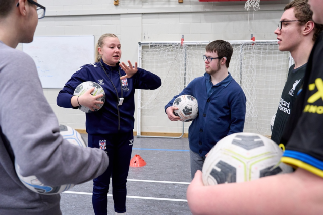 A Sport student is explaining a football activity to the young people stood around them