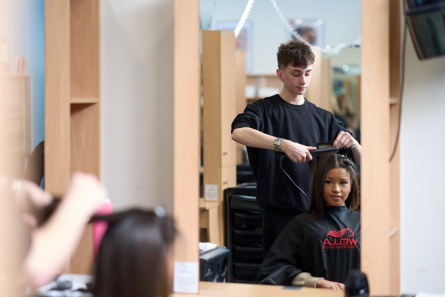 A hairdressing student is straightening a clients hair
