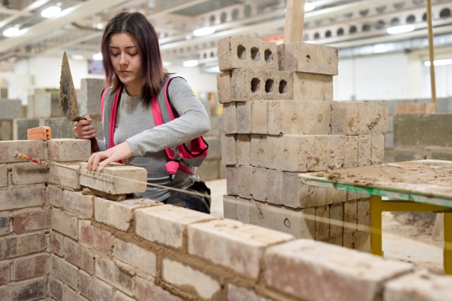 A bricklaying student is placing a brick on some mortar working along a plumbline