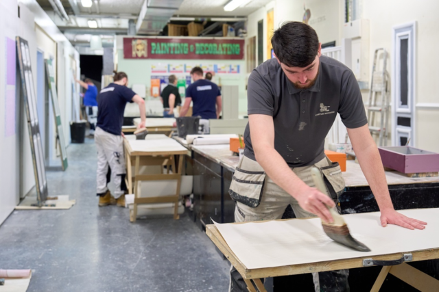 Painting Decorating students are applying paste to wallpaper on pasting tables in the workshop