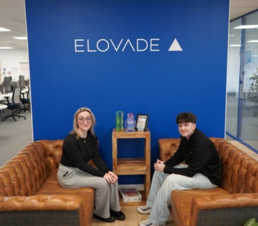 Amy Abba and Josh Jenkins sit on opposing leather sofas in front of Elovade branding in their Thirsk office